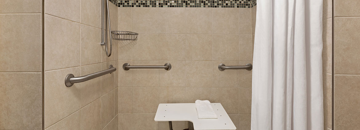 white towels and toliet and easily accessible shower with a sitdown seat